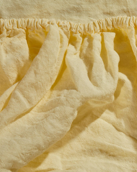Detal elastycznej krawędzi lnianego stonewashed prześcieradła z gumką Sunshine w pastelowym żółtym