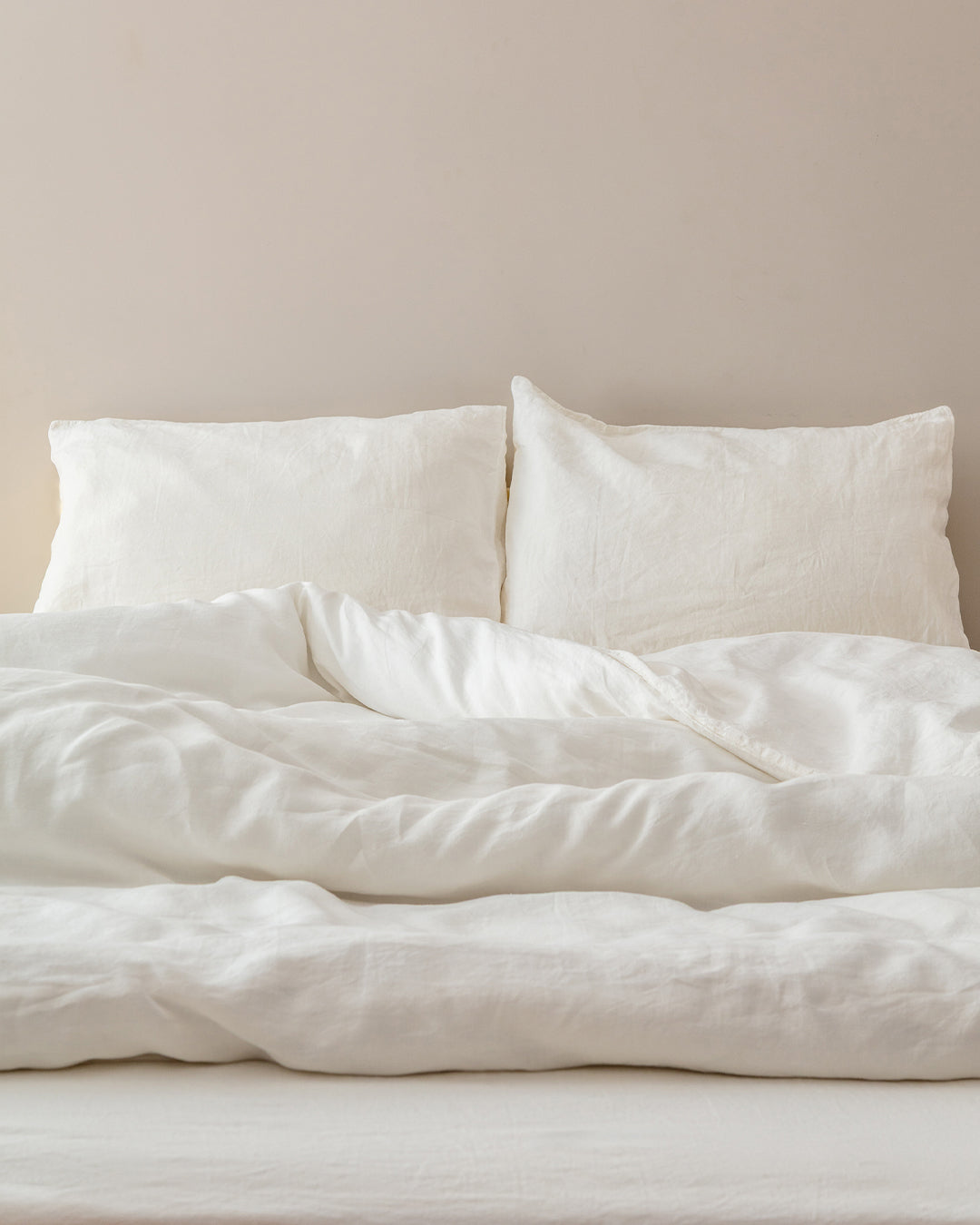 Cream stonewashed flax linen pillowcases and duvet on a styled bed against a neutral wall