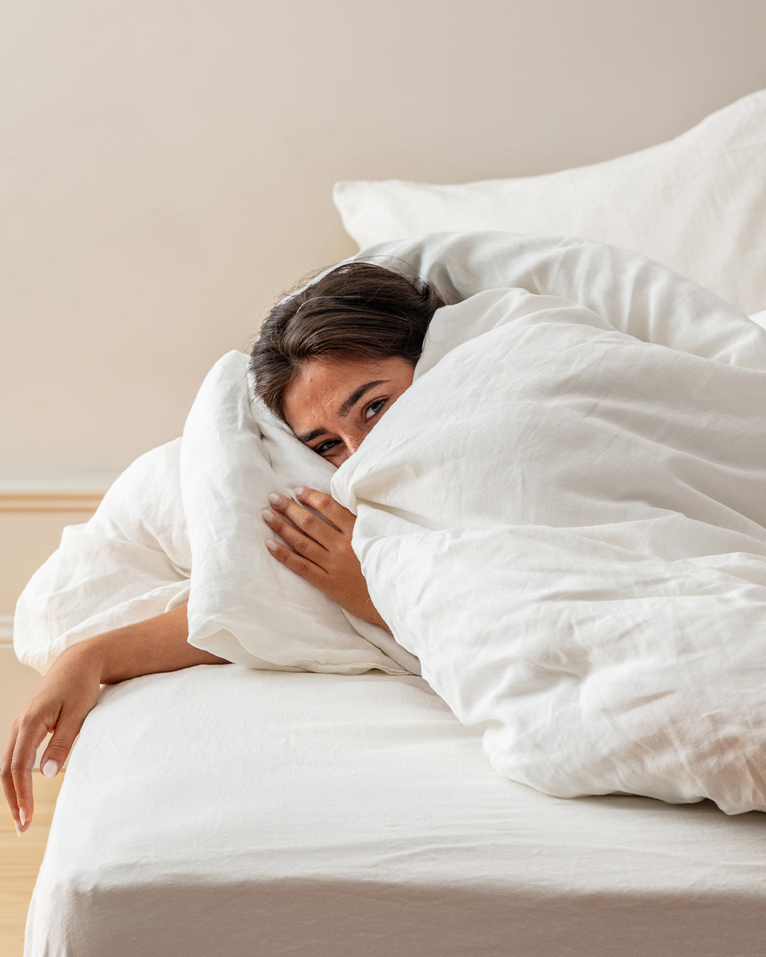 Woman peeking out from under a Cream stonewashed flax linen duvet on a styled bed
