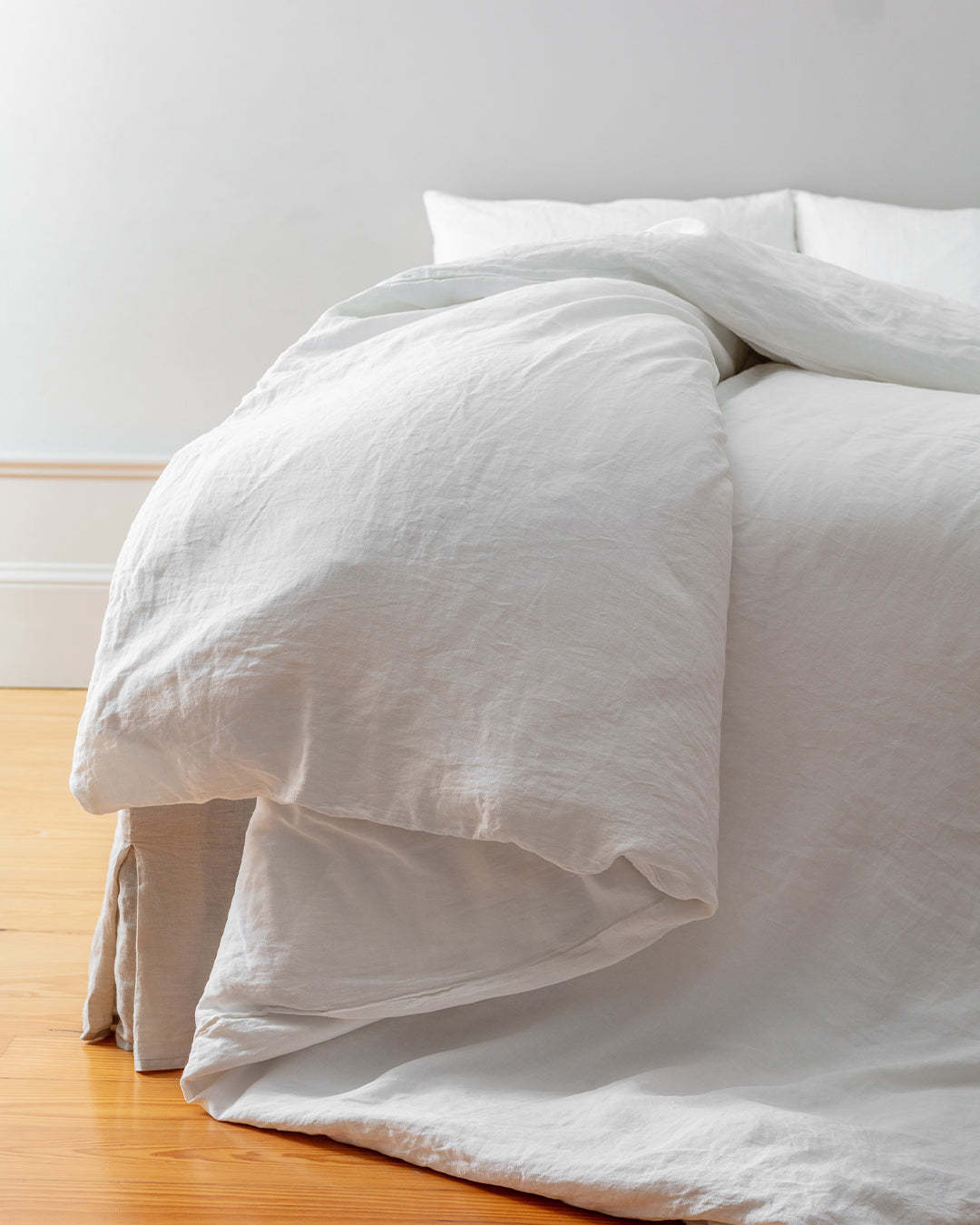 Cream stonewashed flax linen duvet draped over the foot of a bed onto a wooden floor